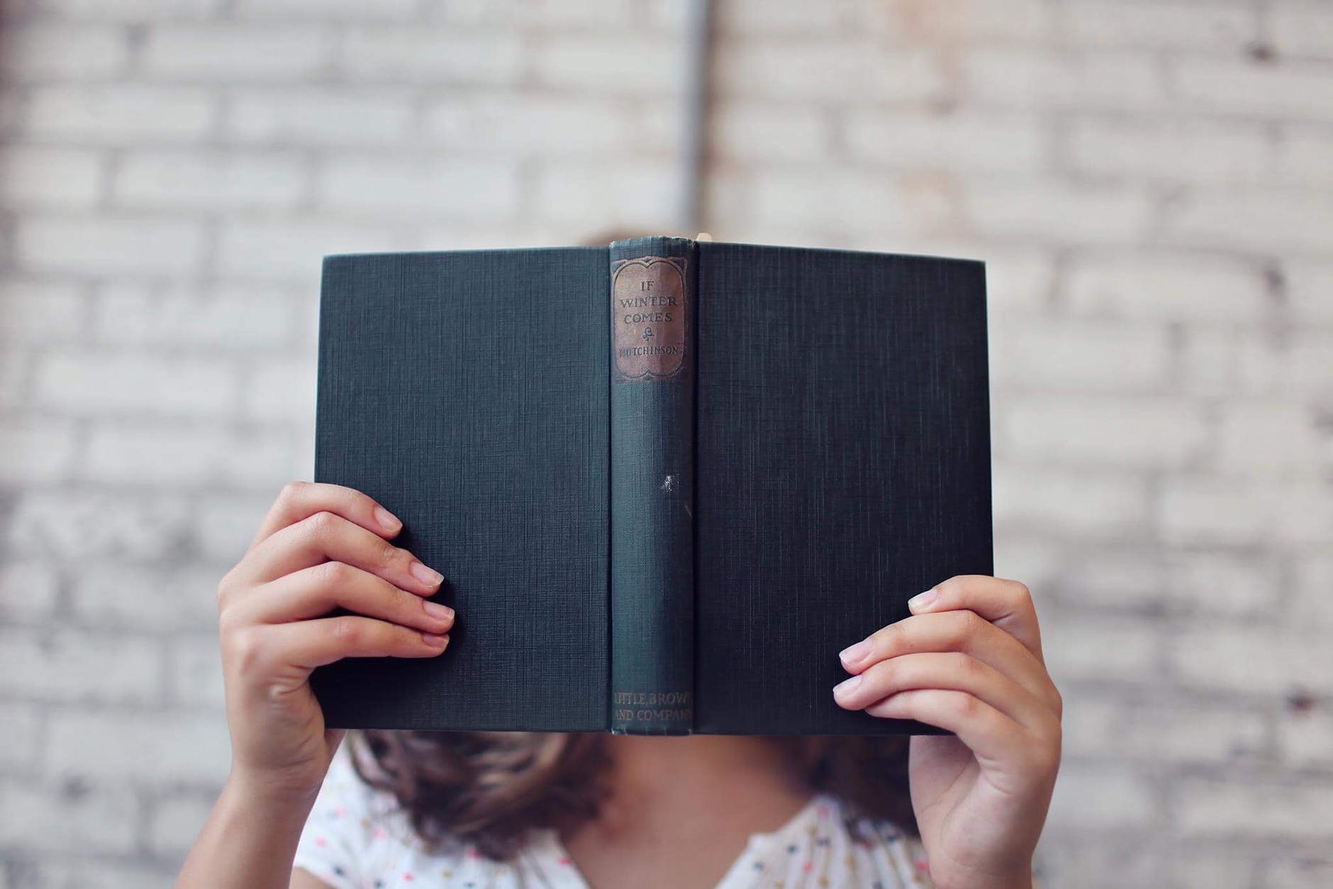 Person holding an open book in front of their face.